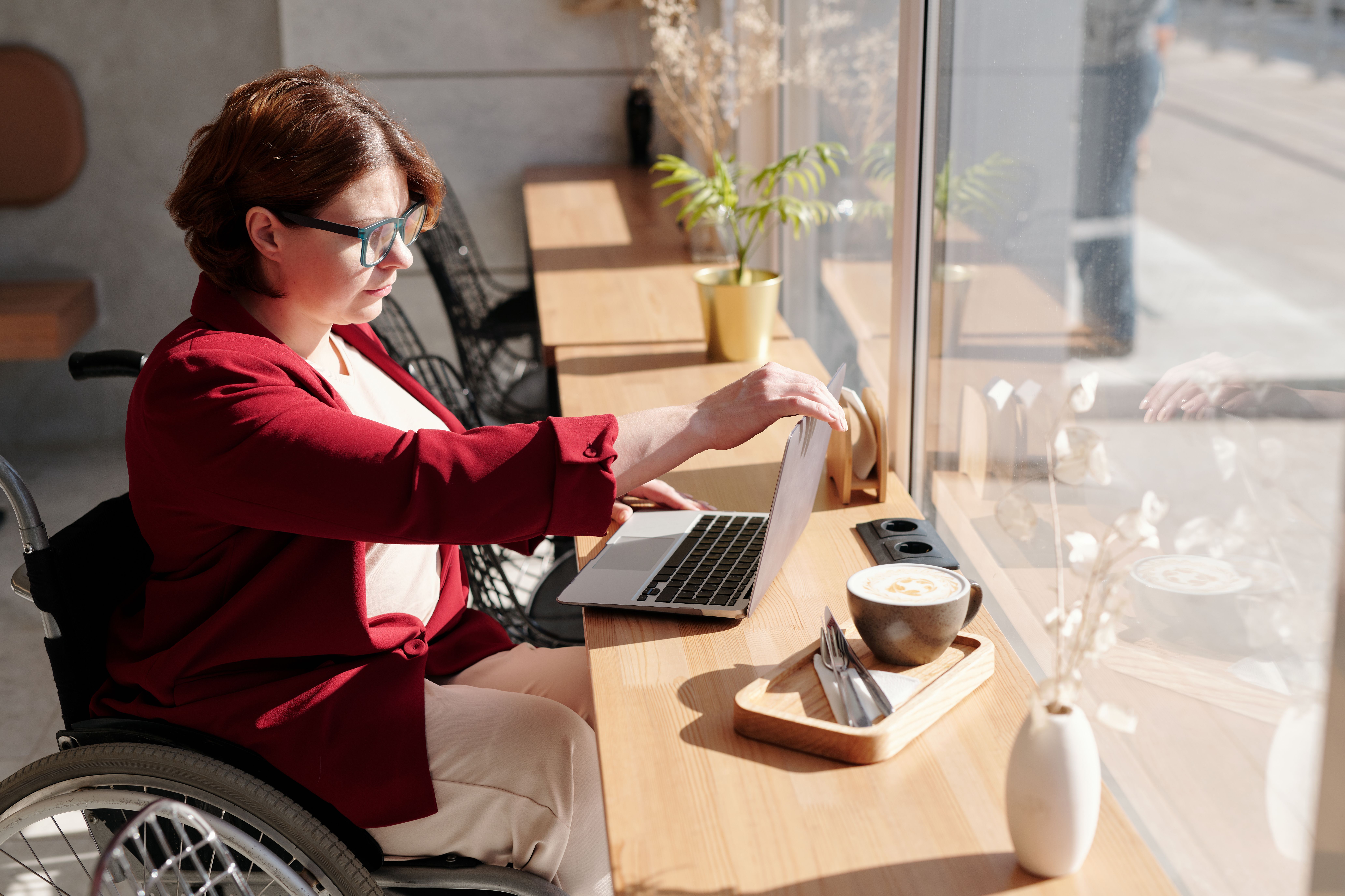 A woman in a wheelchair using a laptop at a café