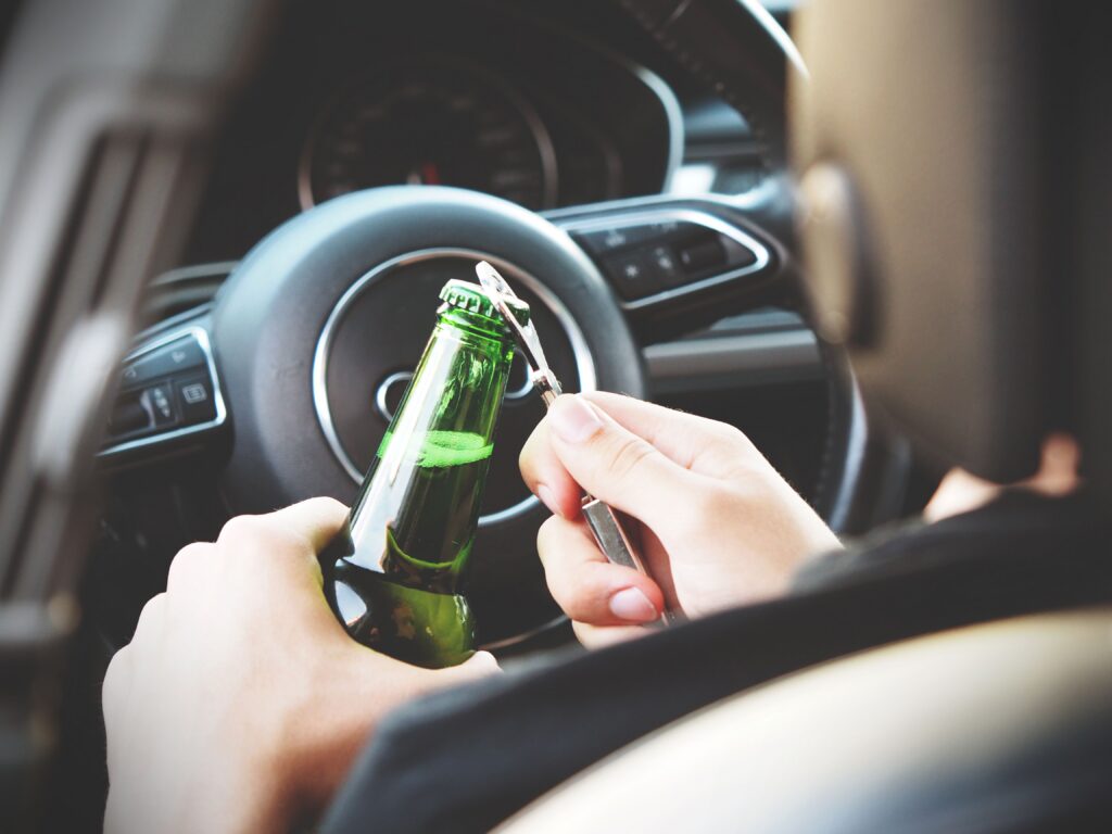 A person opening a bottle inside a vehicle, illustrating concerns about alcohol use and driver safety