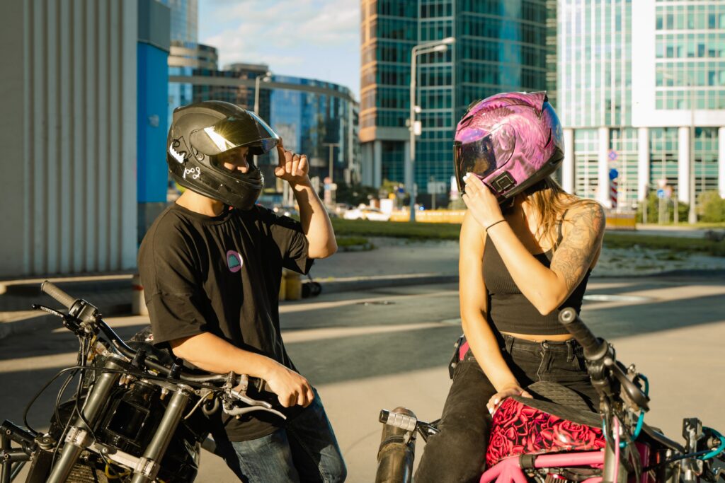 A man and woman lounging by motorcycles while wearing helmets